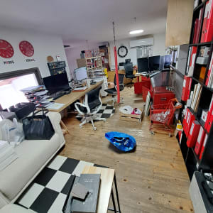 משרד עם שולחנות עבודה, כיסאות ומדפים עם קלסרים אדומים.