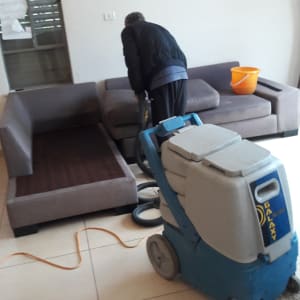 אדם מנקה ספה עם מכונת ניקוי מקצועית