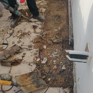 Two workers removing old flooring with tools and debris around.