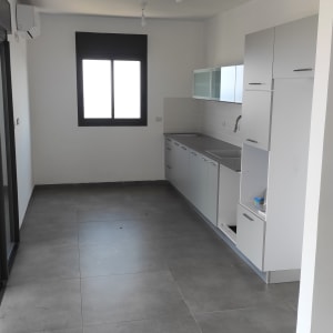 מטבח ריק עם ארונות לבנים ורצפה נקייה