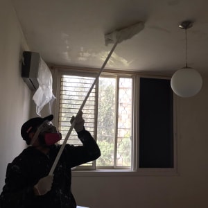 אדם אוטם תקרה עם כלי על מוט ארוך