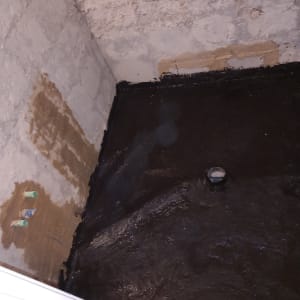 רצפה מצופה בזפת, קיר עם תיקוני טיח, צינור בולט