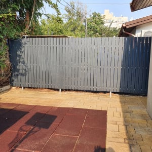 גדר עץ אפורה בחצר עם ריצוף אבן