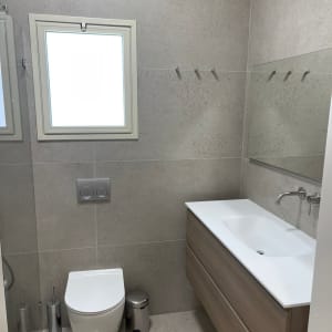 חדר אמבטיה ושירותים מודרני משופץ עם חיפוי אריחים ואסלה תלויה