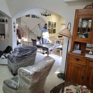 רהיטים עטופים בניילון בבית, אדם עומד ברקע.