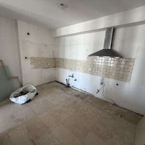 מטבח ריק עם אריחים ישנים ושקית פסולת על הרצפה