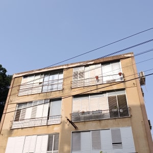 בניין מגורים עם חלונות ותריסים, שמיים כחולים ועצים ברקע