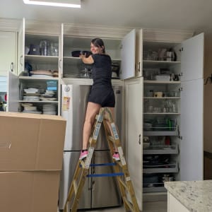 אישה מסדרת ארונות מטבח על סולם