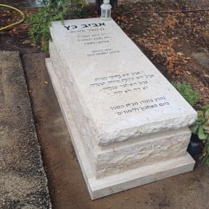 מצבה עם כיתוב בעברית ולצידה עששית לבנה