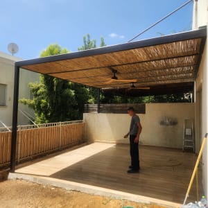 פרגולה מאלומיניום עם כיסוי במבוק וגבר עומד מתחתיה