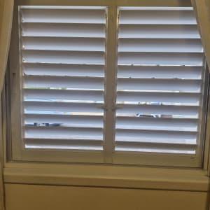 תריסים לבנים על חלון עם וילונות בצדדים