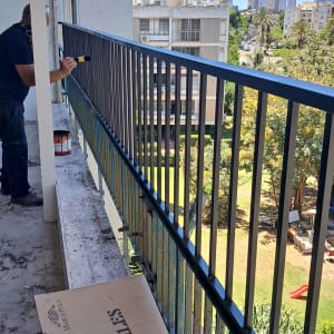 אדם צובע מעקה מתכת במרפסת בניין