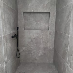 מקלחת עם ראש מקלחת שחור וקירות אריחים אפורים