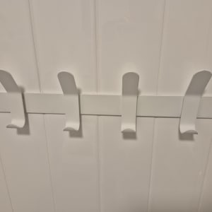 מתלה קיר עם ארבעה ווים על רקע אריחים לבנים