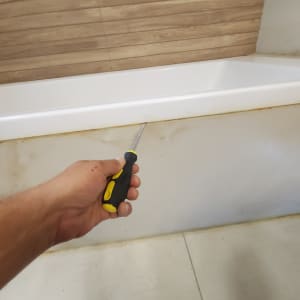 יד מחזיקה מברג ליד אמבטיה עם סימני רטיבות