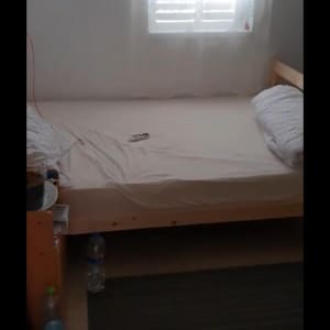 מיטה עם מצעים לבנים ובקבוקי מים על הרצפה