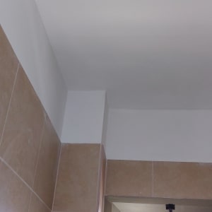 קיר צבוע בלבן ליד חלון עם אריחים חומים