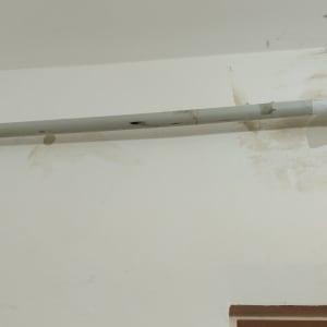 צינור חשמל אפור עם חיבורים על קיר לבן