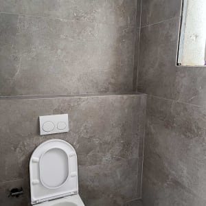 אסלה לבנה בחדר אמבטיה עם קירות אבן אפורים