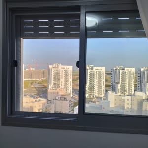 חלון עם תריסים חצי סגורים, נוף עירוני ברקע