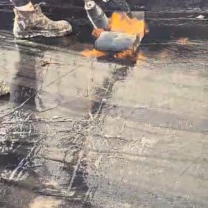 אדם משתמש במבער לאיטום גג עם יריעות ביטומניות