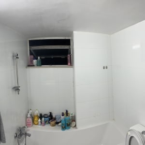 חדר אמבטיה עם אריחים לבנים ומוצרי ניקוי על אדן החלון