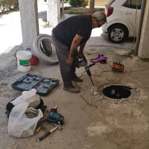 אדם עובד עם מקדחה ליד פתח ביוב