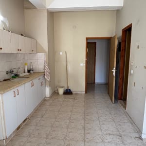 מטבח ריק עם ארונות, כיור ומטאטא בפינה