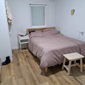 חדר שינה מסודר עם מיטה, שידה ושרפרף עץ