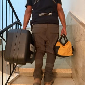 אינסטלטור עולה במדרגות הבניין עם ארגז ותיק כלים