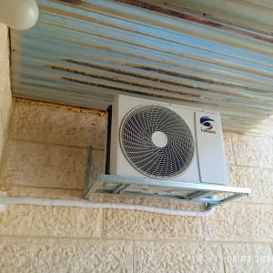 יחידת מיזוג אוויר מותקנת על קיר חיצוני מתחת לגג מתכת.