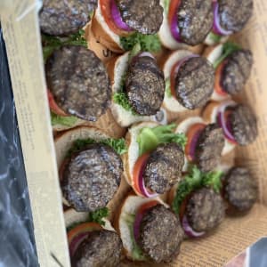 המבורגרים קטנים עם חסה, עגבנייה ובצל באריזת קרטון.