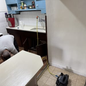 אדם עובד מתחת לכיור במטבח עם צינור ומכשיר