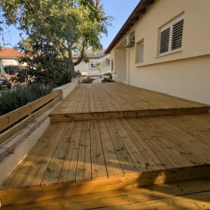 דק עץ בחצר עם עצים ובית ברקע