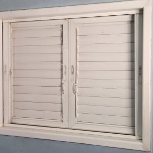 חלון עם תריסים לבנים סגורים ומסגרת לבנה