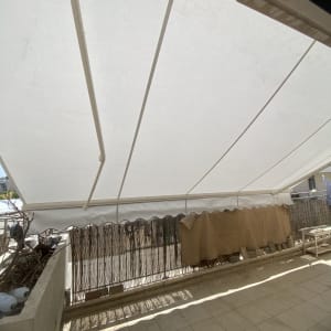 סוכך לבן מתוח מעל מרפסת מרוצפת