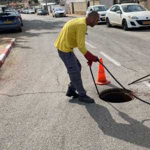 אדם עם צינור ליד פתח ביוב ברחוב