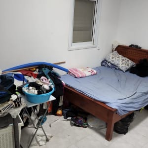 חדר מבולגן עם בגדים על המיטה וסולם בצד