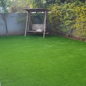 דשא ירוק עם עצים מסביב ונדנדה בגינה