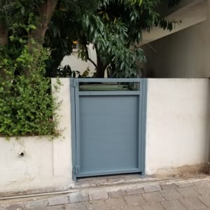 שער מתכת אפור בתוך קיר לבן עם צמחייה מסביב