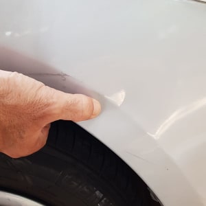 יד מצביעה על שריטה בפגוש רכב לבן