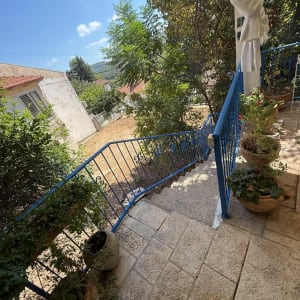 מרפסת מרוצפת אבן ומדרגות חוץ עם מעקה מתכת כחול בבית פרטי