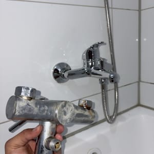 ברז אמבטיה מוחזק ביד ליד קיר אריחים
