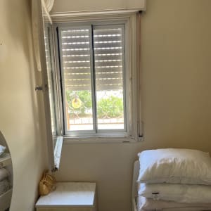 חלון אלומיניום פתוח עם תריסים בחדר שינה.