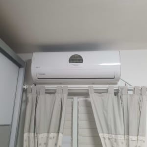 מזגן מותקן על קיר מעל חלון עם וילונות