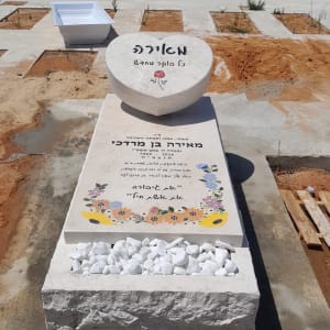 מצבה עם כיתוב פרחים ואבנים לבנות