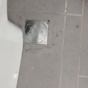 פתח ניקוז מתכת על רצפת אריחים אפורה