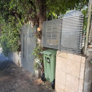 שער מתכת ליד עץ ופח ירוק ברחוב