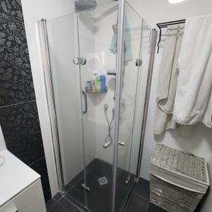 מקלחון זכוכית עם דלתות שקופות ומדף בקבוקים