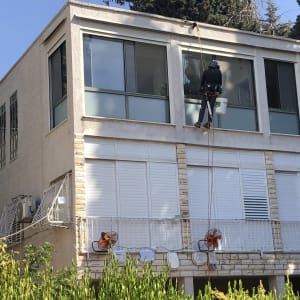 אדם תלוי על חבל מנקה חלונות בקומה עליונה